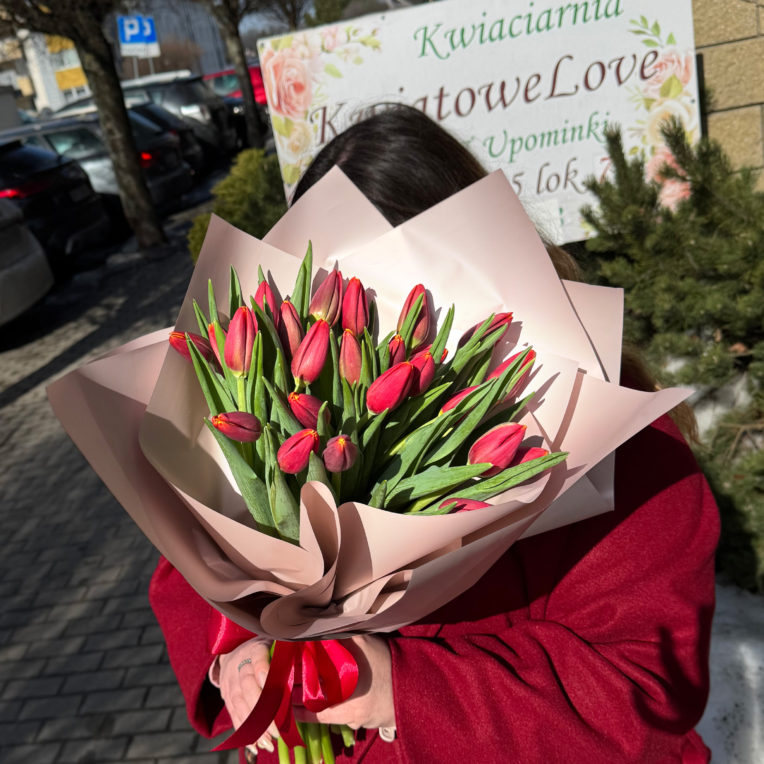 Bukiet z czerwonych tulipanów zapakowany w beżowy papier dekoracyjny z czerwoną kokardką.