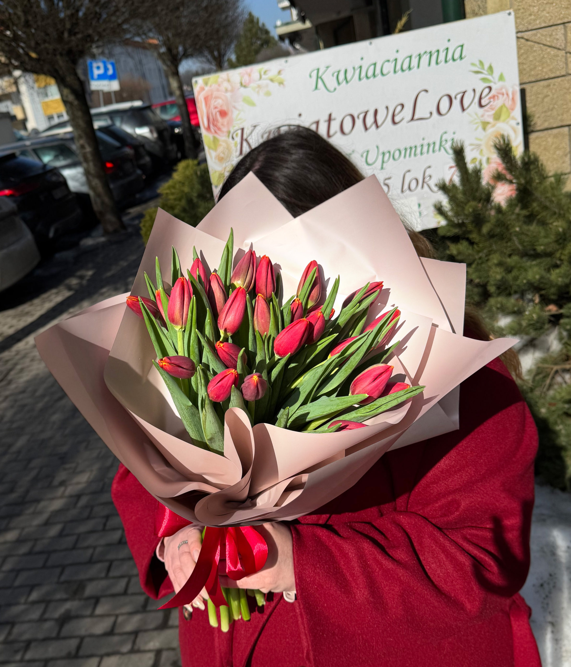 Bukiet z czerwonych tulipanów zapakowany w beżowy papier dekoracyjny z czerwoną kokardką.