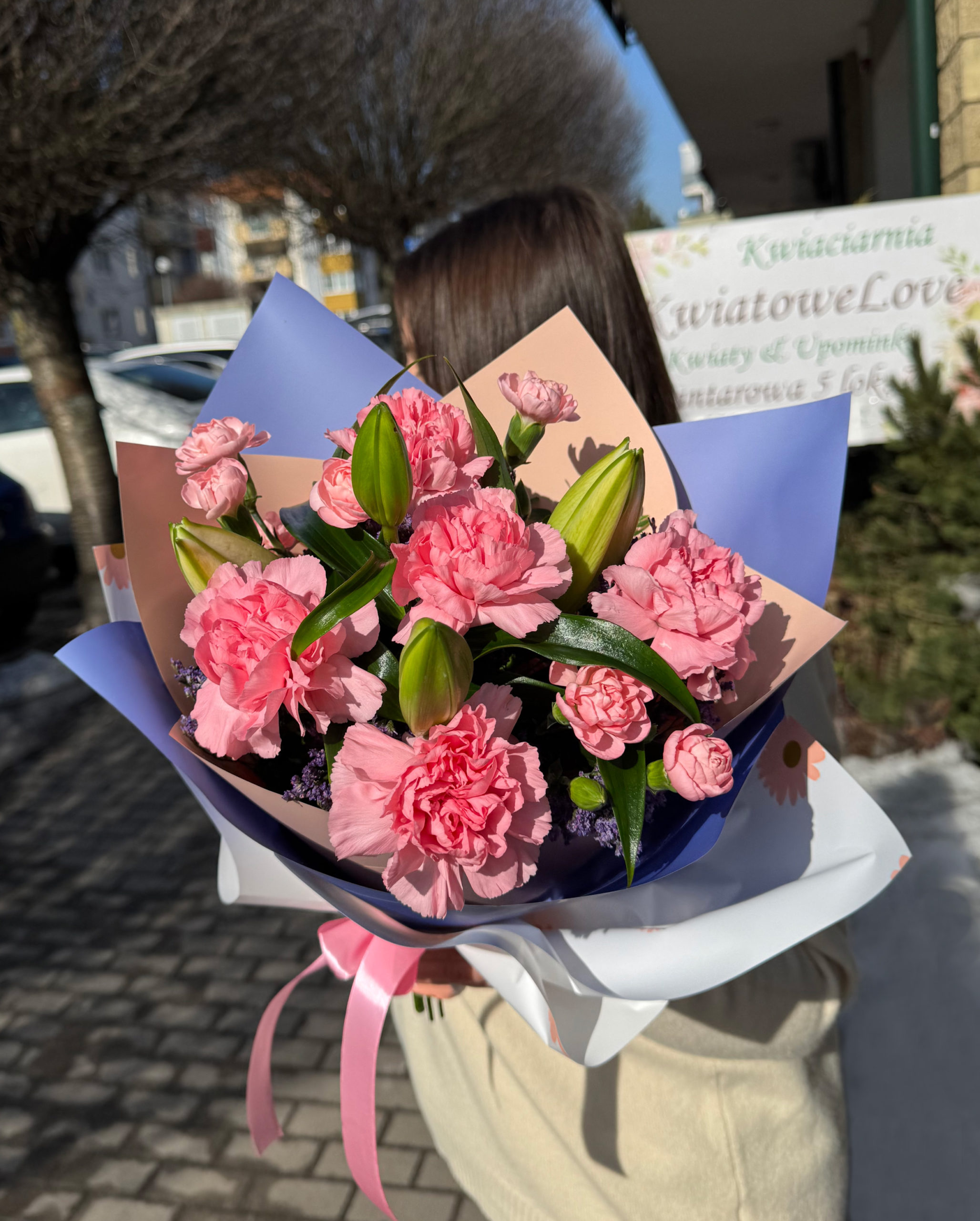 Biało różowo fioletowy bukiet z lilii, różowych goździków i limonium w papierze dekoracyjnym z kokardką