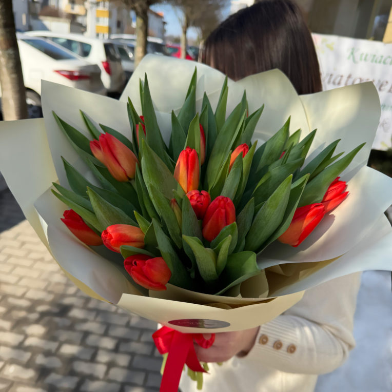 Bukiet czerwono-pomarańczowych tulipanów zapakowany w elegancki kremowy papier ozdobny z czerwoną wstążką