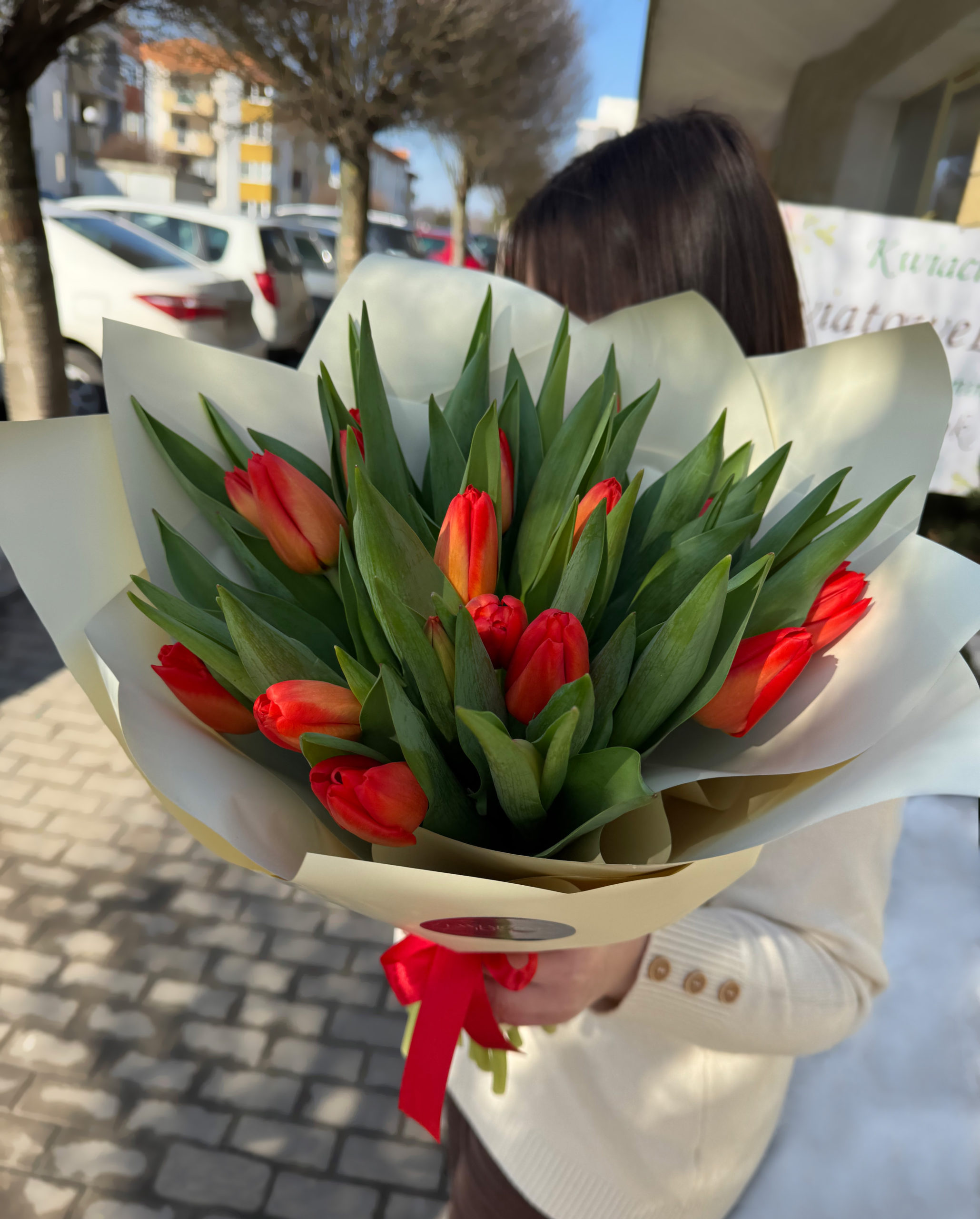 Bukiet czerwono-pomarańczowych tulipanów zapakowany w elegancki kremowy papier ozdobny z czerwoną wstążką