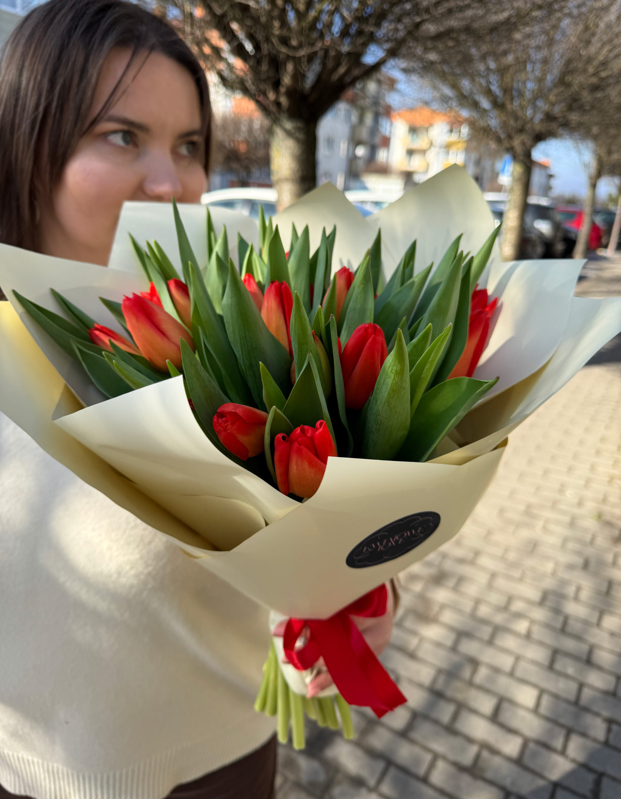 Bukiet czerwono-pomarańczowych tulipanów zapakowany w elegancki kremowy papier ozdobny z czerwoną wstążką